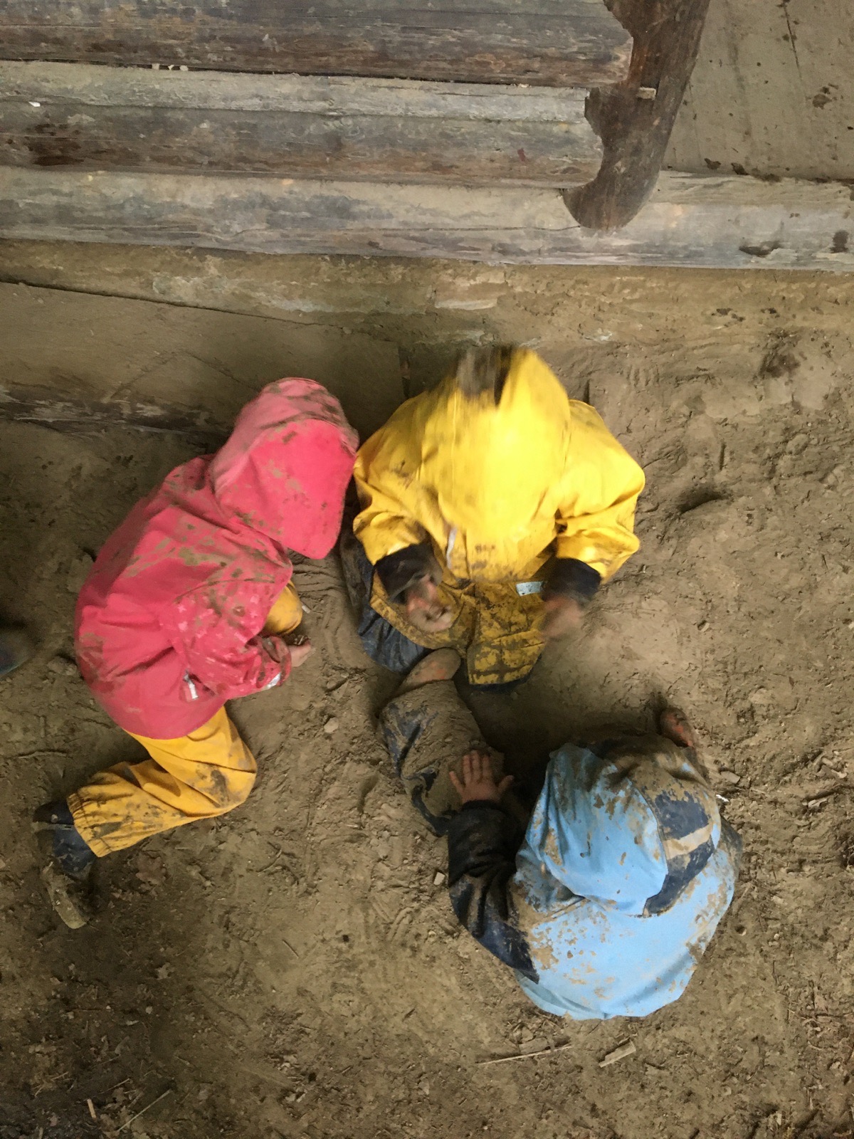 Kinder spielen in Matschkleidung auf dem Waldboden