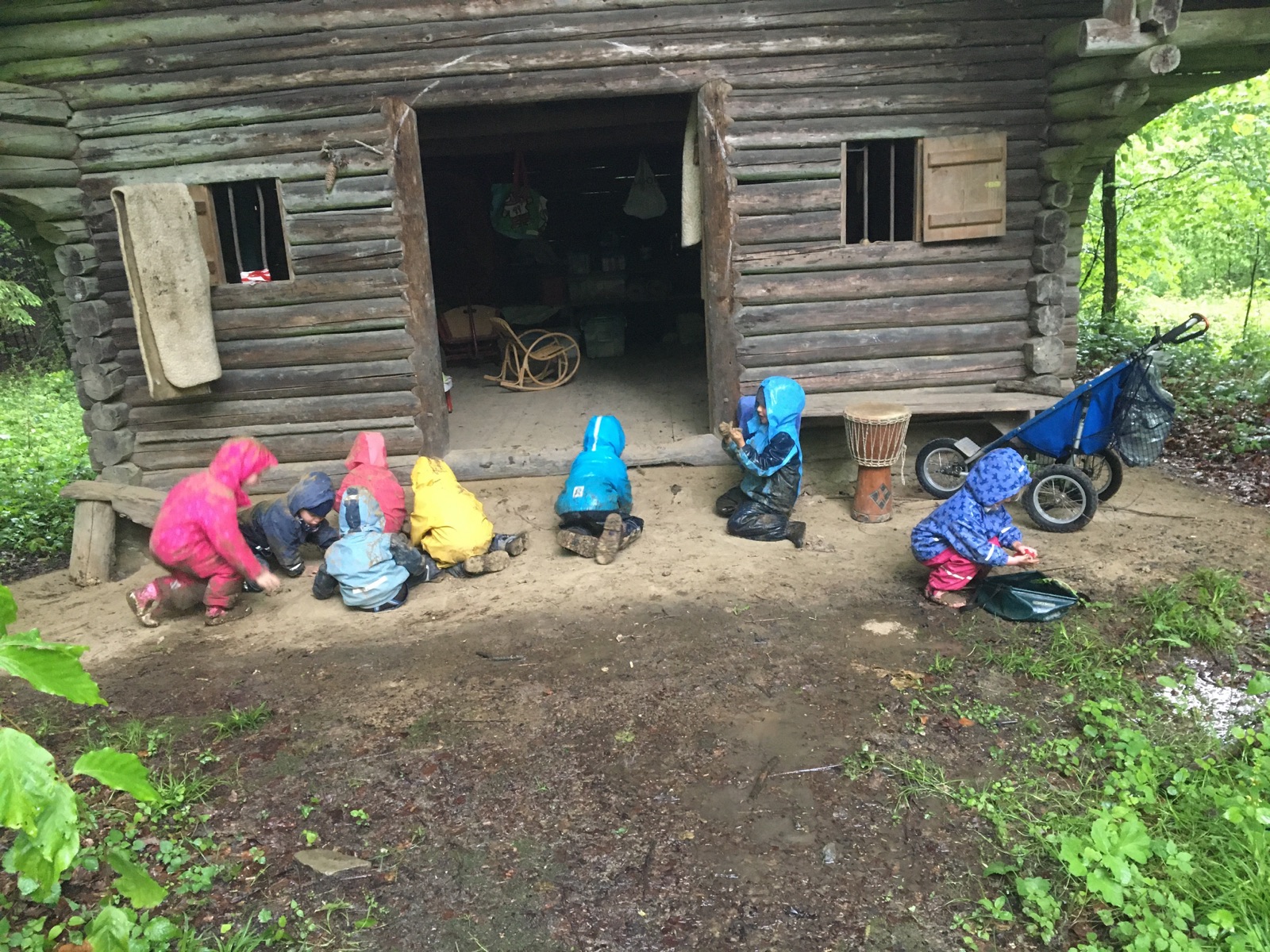 Kinder spielen in Regenkleidung vor der Waldhütte